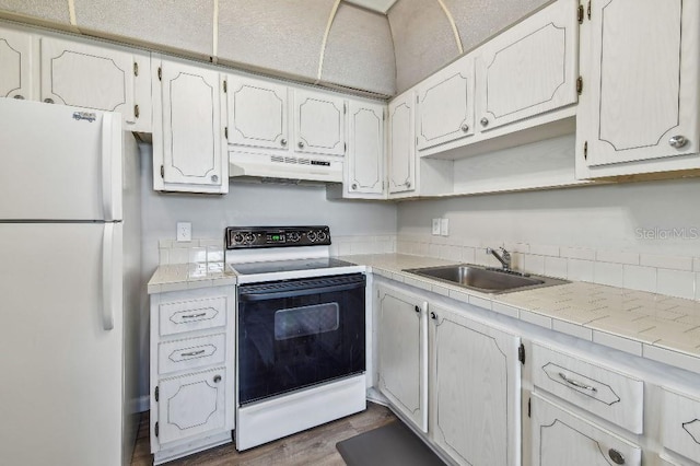 kitchen featuring freestanding refrigerator, electric range, tile counters, under cabinet range hood, and a sink