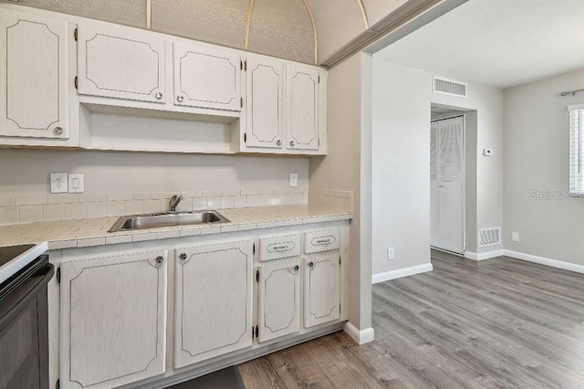 kitchen with visible vents, open shelves, baseboards, a sink, and light wood-style flooring
