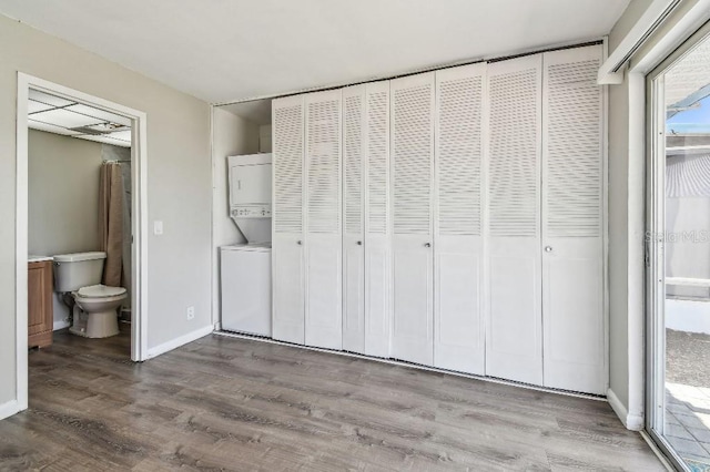 unfurnished bedroom with stacked washer and dryer, wood finished floors, baseboards, connected bathroom, and access to outside