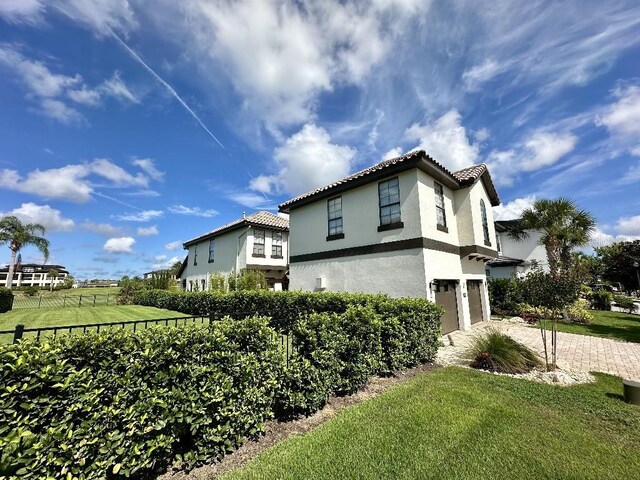view of home's exterior with fence, an attached garage, stucco siding, a lawn, and driveway