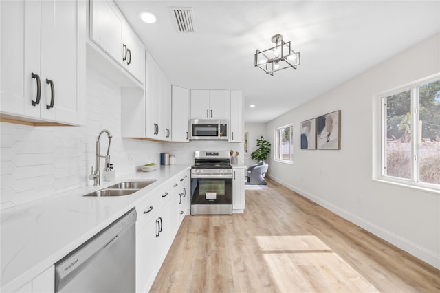 kitchen with appliances with stainless steel finishes, a sink, backsplash, light wood-style flooring, and baseboards