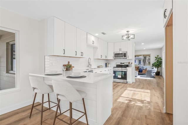 kitchen with appliances with stainless steel finishes, a sink, light wood finished floors, decorative backsplash, and light countertops