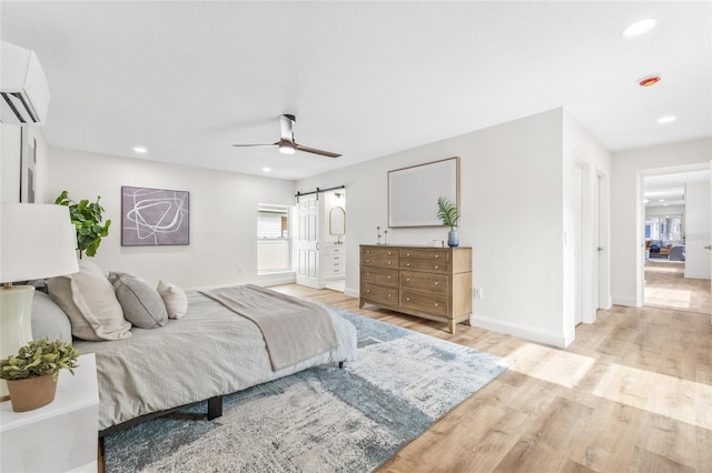 bedroom with a barn door, light wood-style flooring, baseboards, a wall mounted air conditioner, and recessed lighting