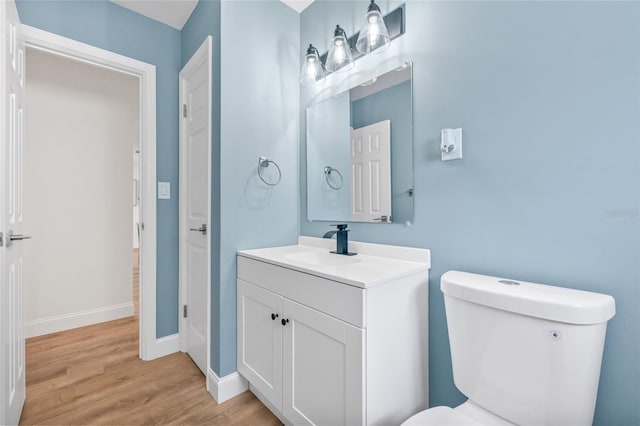 half bathroom with wood finished floors, toilet, baseboards, and vanity