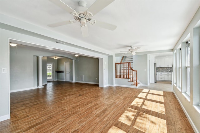 unfurnished living room featuring visible vents, a ceiling fan, decorative columns, and stairway