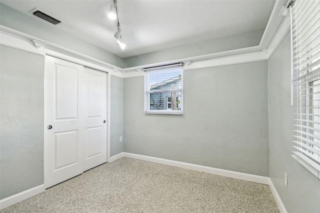 unfurnished bedroom with visible vents, baseboards, speckled floor, and track lighting