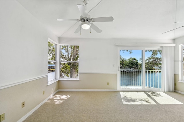 carpeted empty room featuring baseboards, a water view, and a ceiling fan