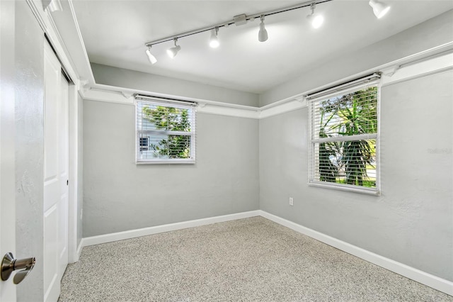 spare room with baseboards, rail lighting, and speckled floor