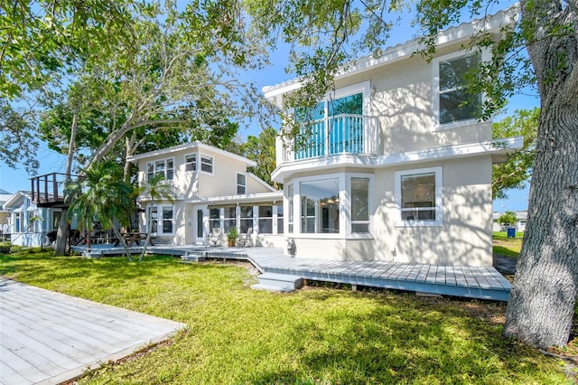 rear view of property with a wooden deck, stucco siding, a yard, and a balcony
