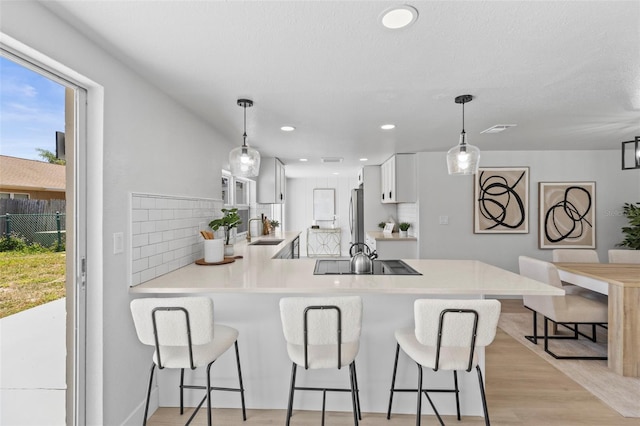 kitchen featuring freestanding refrigerator, a peninsula, a kitchen bar, black electric cooktop, and a sink