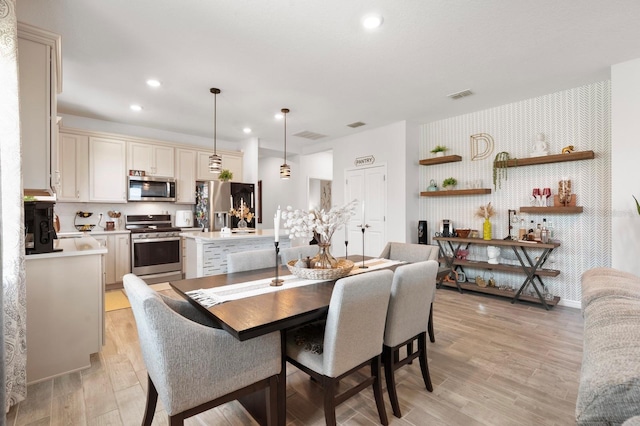 dining area featuring light wood finished floors, an accent wall, recessed lighting, wallpapered walls, and visible vents