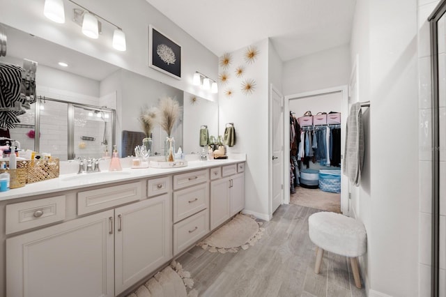 bathroom with double vanity, wood finished floors, a walk in closet, a shower stall, and a sink