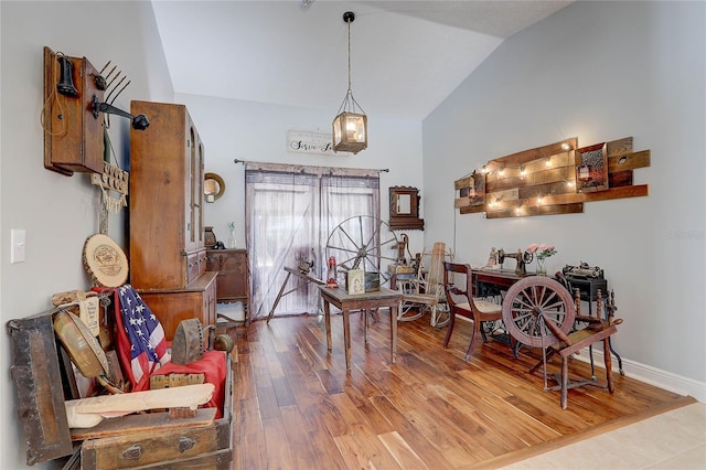 dining space featuring baseboards, wood finished floors, and high vaulted ceiling
