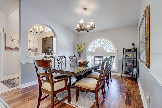 dining area featuring arched walkways, baseboards, a chandelier, and wood finished floors