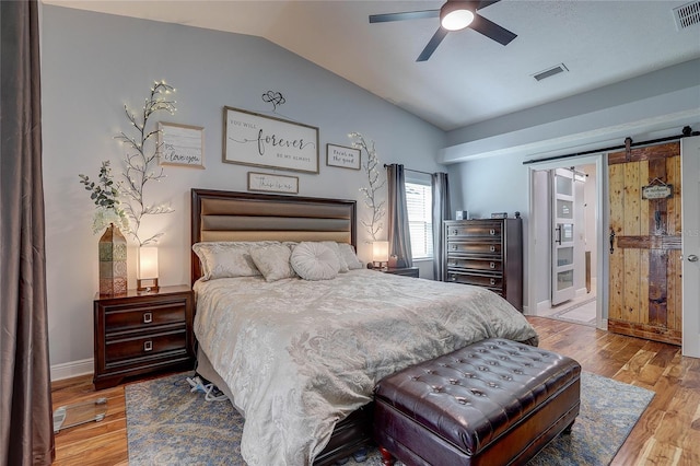 bedroom featuring wood finished floors, vaulted ceiling, a barn door, and visible vents