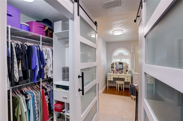 spacious closet featuring tile patterned flooring, a barn door, and visible vents