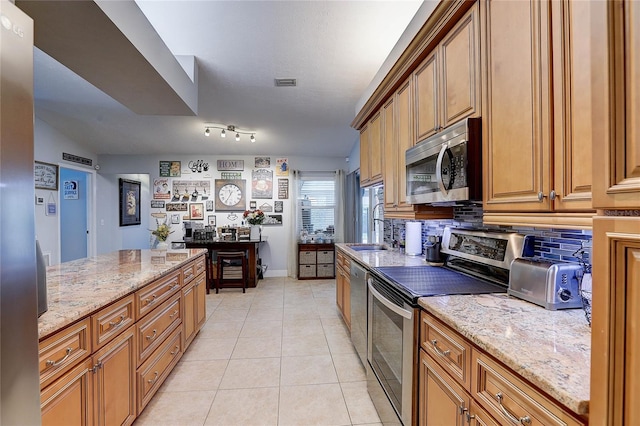 kitchen with light tile patterned flooring, light stone countertops, brown cabinets, tasteful backsplash, and stainless steel appliances