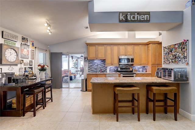 kitchen with appliances with stainless steel finishes, a breakfast bar area, brown cabinets, and light stone countertops