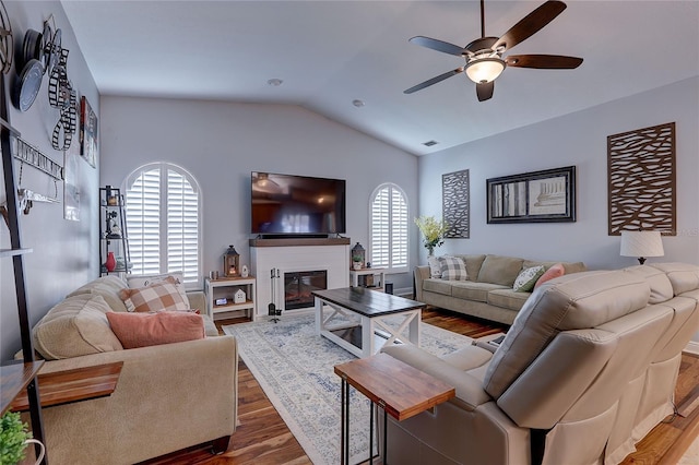 living room featuring a ceiling fan, visible vents, vaulted ceiling, wood finished floors, and a glass covered fireplace