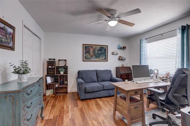 home office with baseboards, a ceiling fan, light wood finished floors, and a textured ceiling