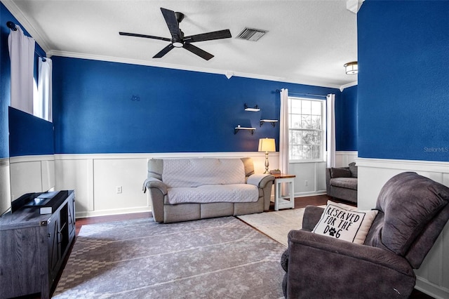 living room featuring visible vents, ornamental molding, a decorative wall, a wainscoted wall, and a ceiling fan