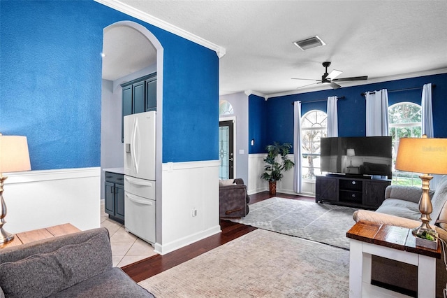 living room with visible vents, a ceiling fan, ornamental molding, light wood-style floors, and arched walkways