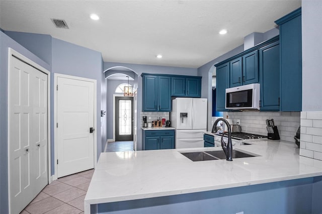 kitchen featuring blue cabinetry, arched walkways, white refrigerator with ice dispenser, a sink, and a peninsula
