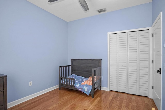 bedroom with baseboards, a closet, wood finished floors, and visible vents