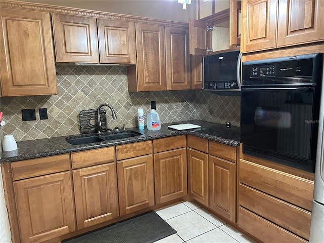 kitchen featuring a sink, dark stone counters, black oven, and backsplash