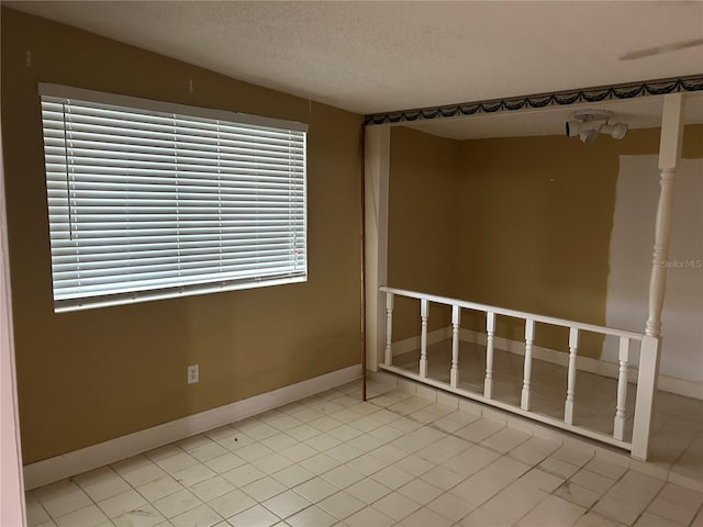 tiled empty room featuring baseboards and a textured ceiling
