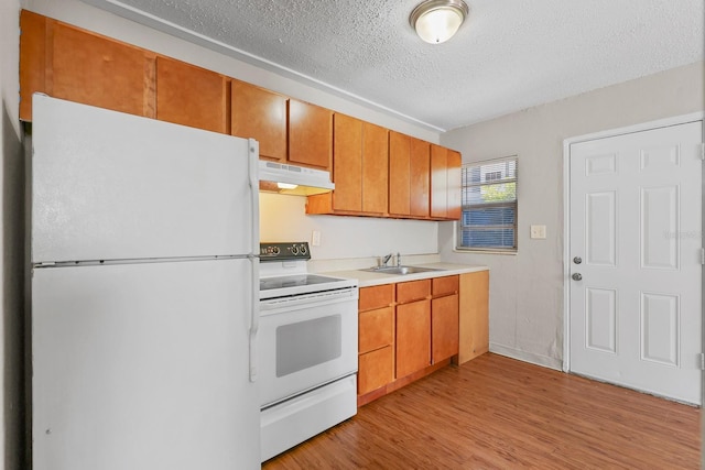 kitchen with a textured ceiling, a sink, light wood finished floors, under cabinet range hood, and white appliances