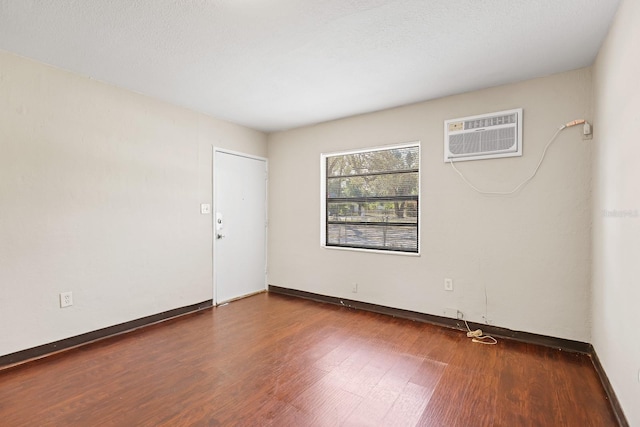 spare room featuring baseboards, a wall mounted AC, and wood finished floors