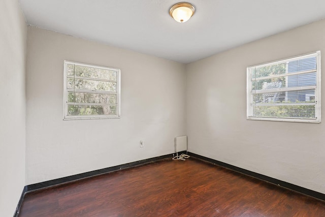 spare room with baseboards and dark wood-style flooring