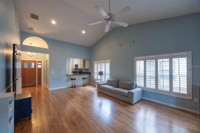 living room featuring high vaulted ceiling, a ceiling fan, baseboards, wood finished floors, and visible vents