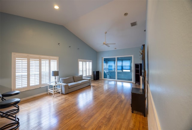 living area featuring ceiling fan, light wood-style floors, high vaulted ceiling, baseboards, and visible vents