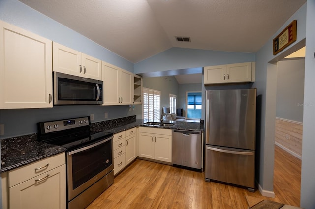 kitchen featuring lofted ceiling, light wood-style floors, dark stone counters, a sink, and appliances with stainless steel finishes