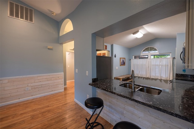kitchen featuring a sink, visible vents, baseboards, wood finished floors, and vaulted ceiling
