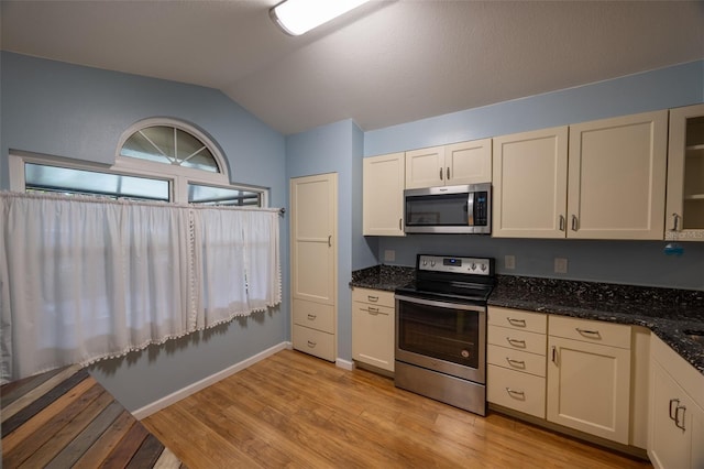 kitchen featuring vaulted ceiling, dark stone countertops, stainless steel appliances, and light wood-type flooring