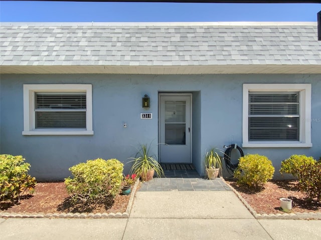 3311 Teeside Dr, New Port Richey, FL 34655 - entrance to property featuring roof with shingles, stucco siding, and mansard roof