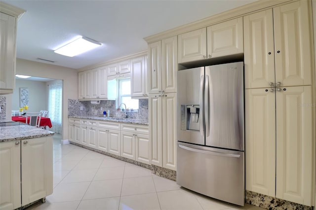kitchen featuring decorative backsplash, a sink, stainless steel fridge with ice dispenser, light stone counters, and cream cabinetry