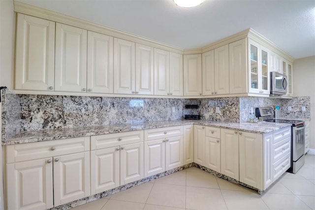 kitchen with backsplash, cream cabinets, light stone countertops, stainless steel appliances, and light tile patterned flooring
