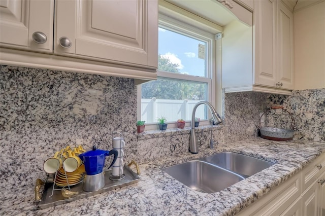 kitchen featuring plenty of natural light, a sink, light stone countertops, and tasteful backsplash