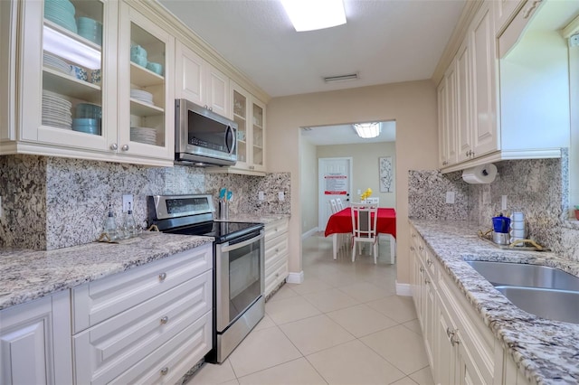 kitchen featuring stainless steel appliances, light tile patterned floors, backsplash, visible vents, and glass insert cabinets