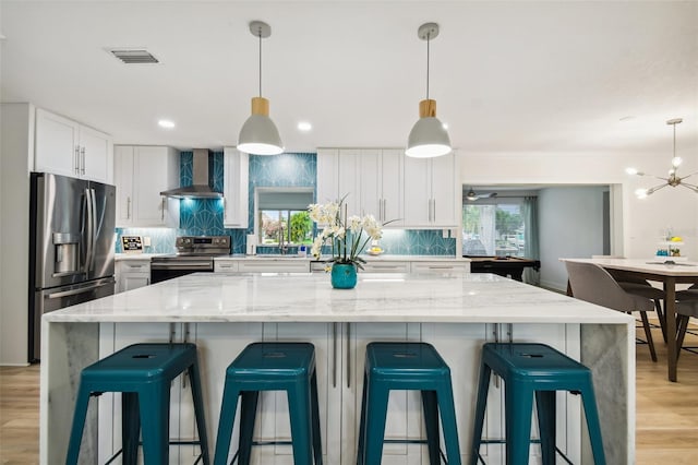 kitchen featuring wall chimney range hood, decorative backsplash, visible vents, appliances with stainless steel finishes, and white cabinets
