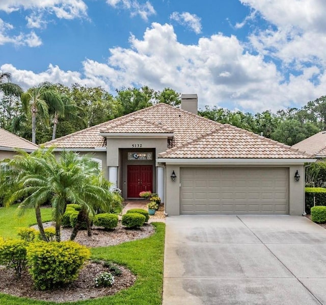 view of front facade with an attached garage, a tile roof, stucco siding, a chimney, and driveway