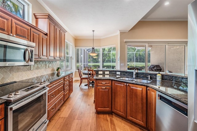 kitchen featuring appliances with stainless steel finishes, a sink, light wood finished floors, plenty of natural light, and decorative backsplash
