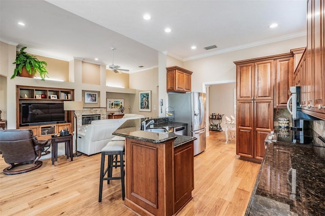 kitchen featuring ceiling fan, a breakfast bar area, a stone fireplace, visible vents, and ornamental molding
