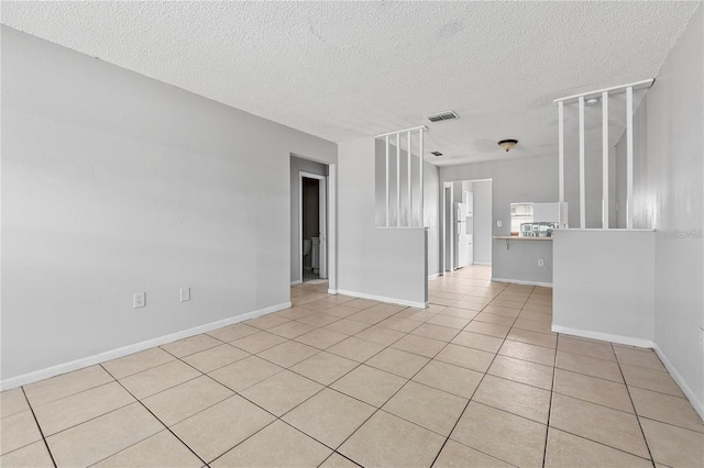 spare room featuring a textured ceiling, baseboards, light tile patterned flooring, and visible vents