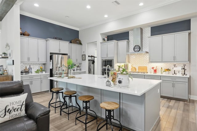 21746 Amelia Rose Way, Land O Lakes, FL 34637 - kitchen with a breakfast bar area, decorative backsplash, wall chimney range hood, light wood-style floors, and appliances with stainless steel finishes