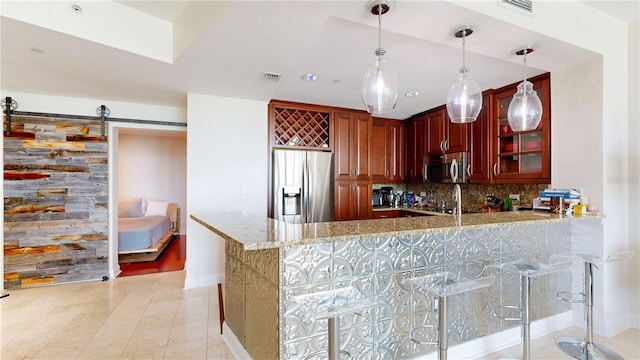 kitchen with light stone countertops, a barn door, stainless steel appliances, a peninsula, and tasteful backsplash